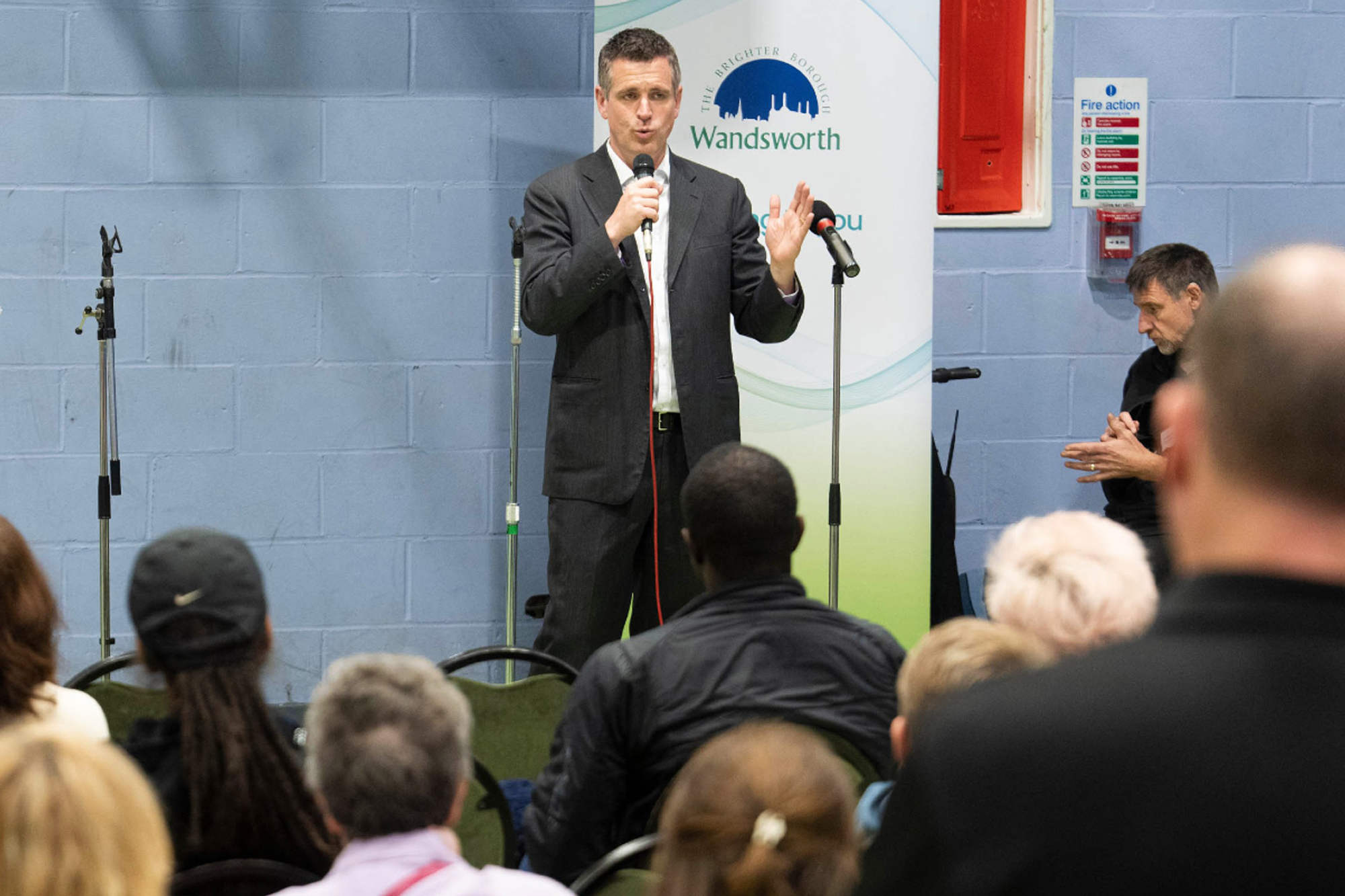 Wandsworth Council Leader Simon Hogg is pictured at a microphone, in front of a community audience, answering questions