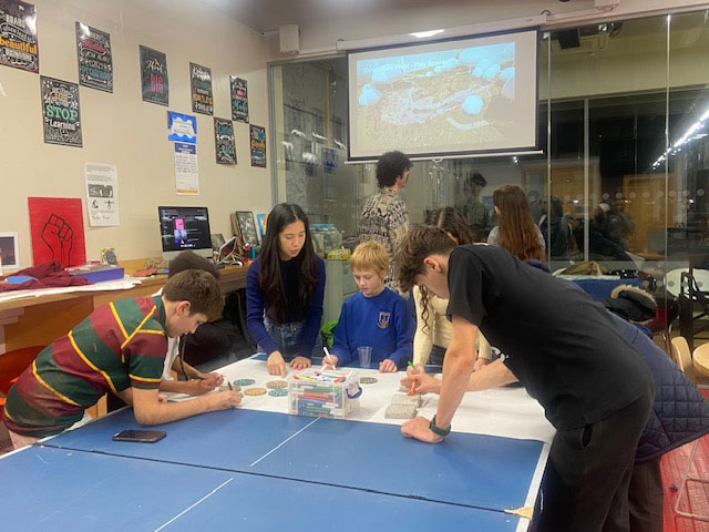 Members of the Youth Advisory Panel are pictured here, standing around a table examining objects, at the second workshop event